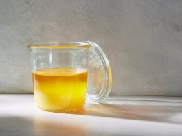 A glass jar filled with a golden yellow liquid, with a glass lid leaning against it.