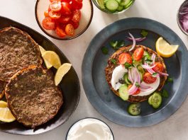 A platter of pitas with ground meat cooked onto them sits next to a plate with a single serving topped with tomatoes.