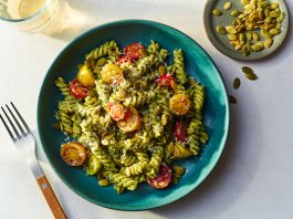 A close-up image of a blue bowl of mafaldine pasta in tomato sauce, with spinach meatballs. There is a fork in the bowl breaking apart one of the meatballs.