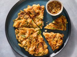 Squares of gamja jeon sit on a pale plate. A pair of chopsticks dip one piece into a sauce.