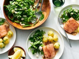 Plates hold salmon, potatoes and salad next to a larger salad bowl.