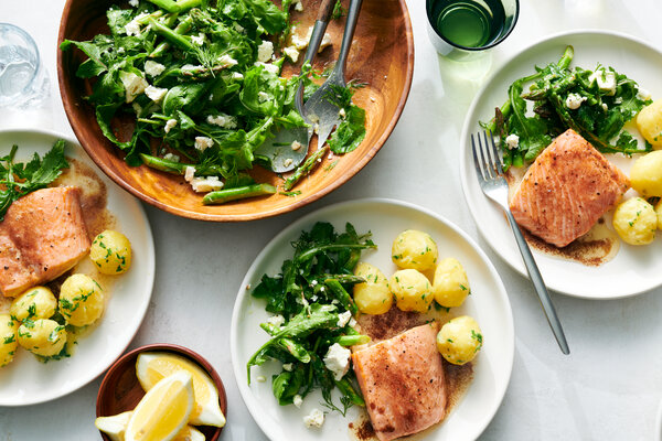 Plates hold salmon, potatoes and salad next to a larger salad bowl.