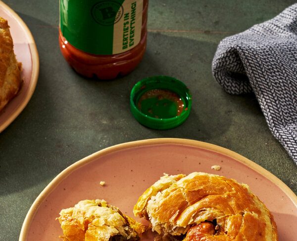A beef patty torn open to expose its filling on a plate. A bottle of hot sauce and a napkin are in the background.