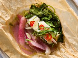 A fork sliced into a piece of fish cooked in parchment with greens and radish.