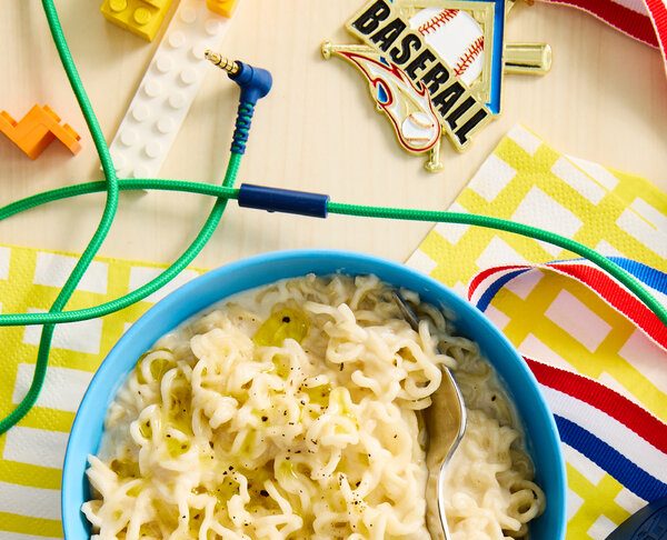 A bowl of chicken and kale topped with sliced avocado is surrounded by toys.