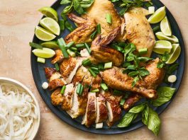 A chicken carved on a platter, topped with herbs and next to lime wedges.