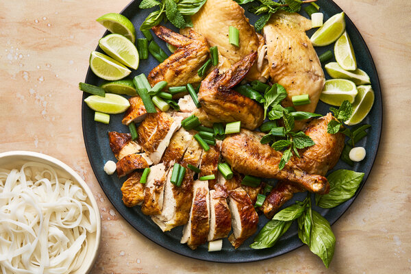 A chicken carved on a platter, topped with herbs and next to lime wedges.