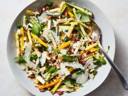 Thin batons of zucchini tossed with cheese and nuts in a white platter.
