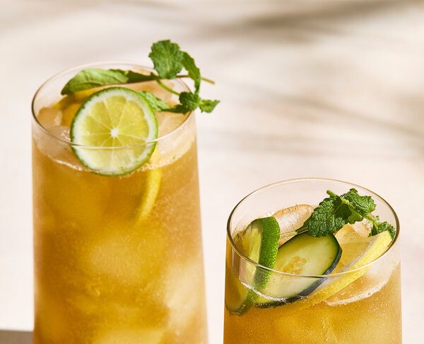 Two tall, clear glasses of a Pimm’s cup photographed at an angle.