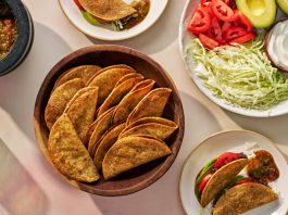 A bowl of crisp tacos is surrounded by a platter of fixings and a bowl of salsa.