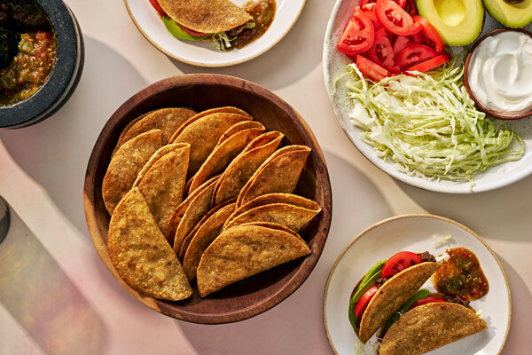 A bowl of crisp tacos is surrounded by a platter of fixings and a bowl of salsa.