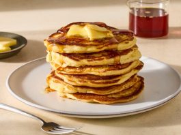 A tall stack of pancakes with butter and maple syrup on top. 