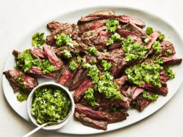 An overhead image of a sliced steak topped with an herb sauce.