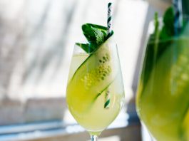 A Hugo spritz in a wine glass, garnished with mint and a thin ribbon of cucumber.