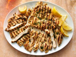An overhead image of sliced chicken breast on a platter next to lemon wedges.