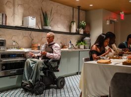 The Chef Imagining a More Accessible World, One Meal at a Time Lay Alston, in a wheelchair, looks at the camera from an open kitchen. She has short, blonde hair and wears a dark vest, light shirt and blue jeans.
