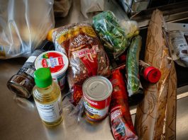 I Create Recipes for a Living. Here’s How I Fed My Family Really Well for $28 a Day. A person in a blue shirt and another in a striped top, both with focused expressions, look at a paper in a grocery store aisle.