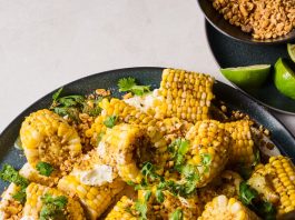 An overhead image of corn cobs on a platter, sprinkled with a spice mix and herbs.