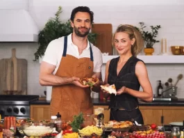 Tom Bateman with Lili Reinhart at a kitchen counter filled with pizza toppings.